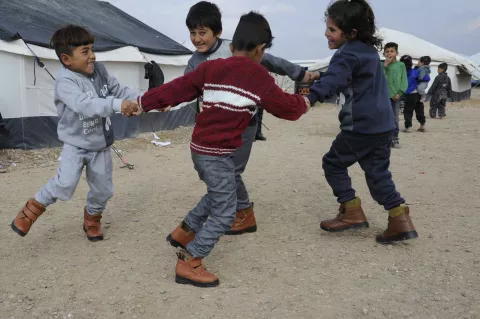 Four children dancing in circle and holding eachothers hand outside, in a camp